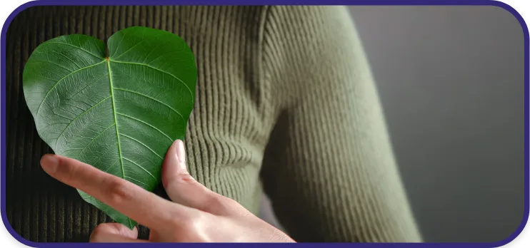 A person holding a heart-shaped leaf in front of their chest, symbolizing eco-friendly values